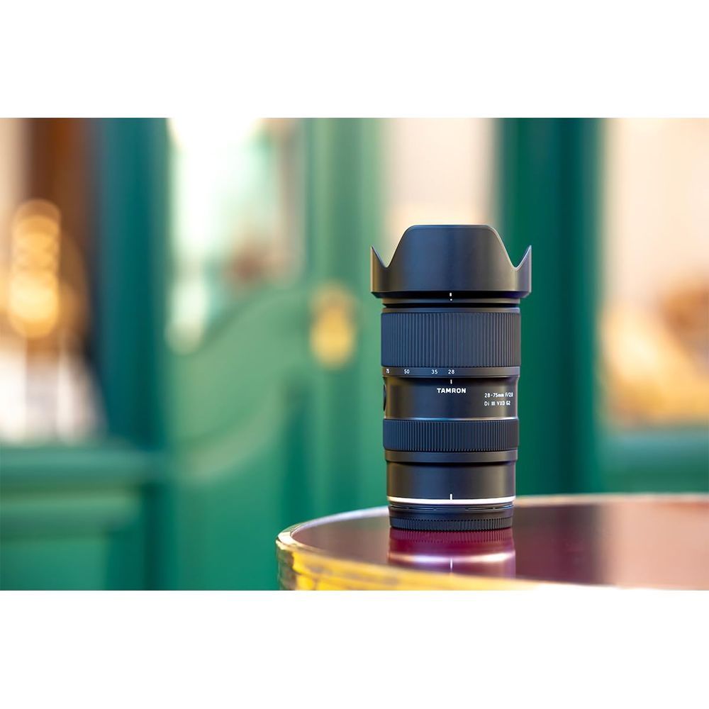 Tamron Kameraobjektiv mit Gegenlichtblende auf glänzendem Tisch.