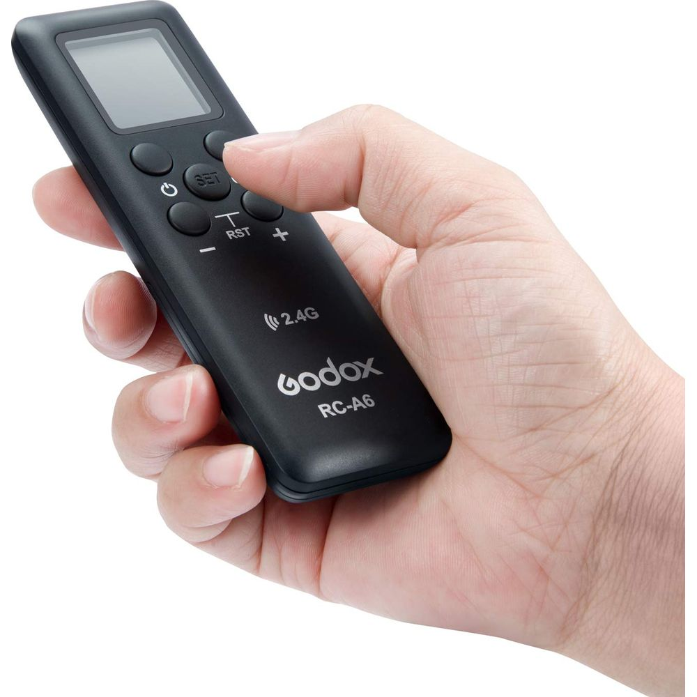 Eine Hand hält eine schwarze Godox RC-A6 Fernbedienung mit Digitalanzeige.
