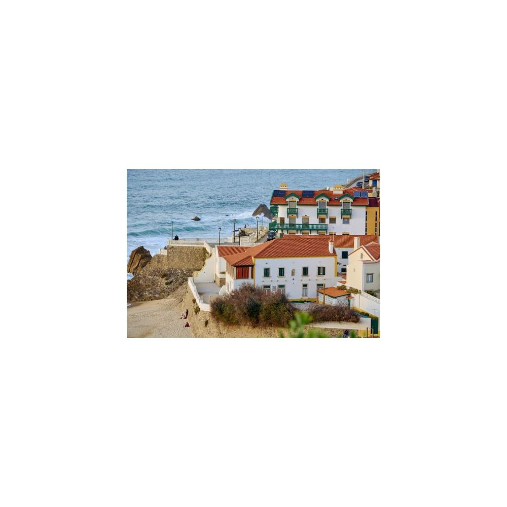 Weiße Häuser mit roten Ziegeldächern am Meer mit Felsen und Strand.