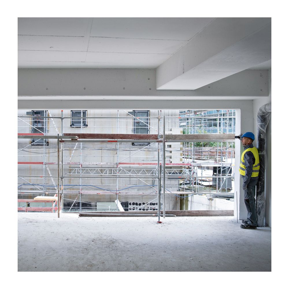 Ein Bauarbeiter in Warnweste blickt auf eine Baustelle mit Gerüsten.