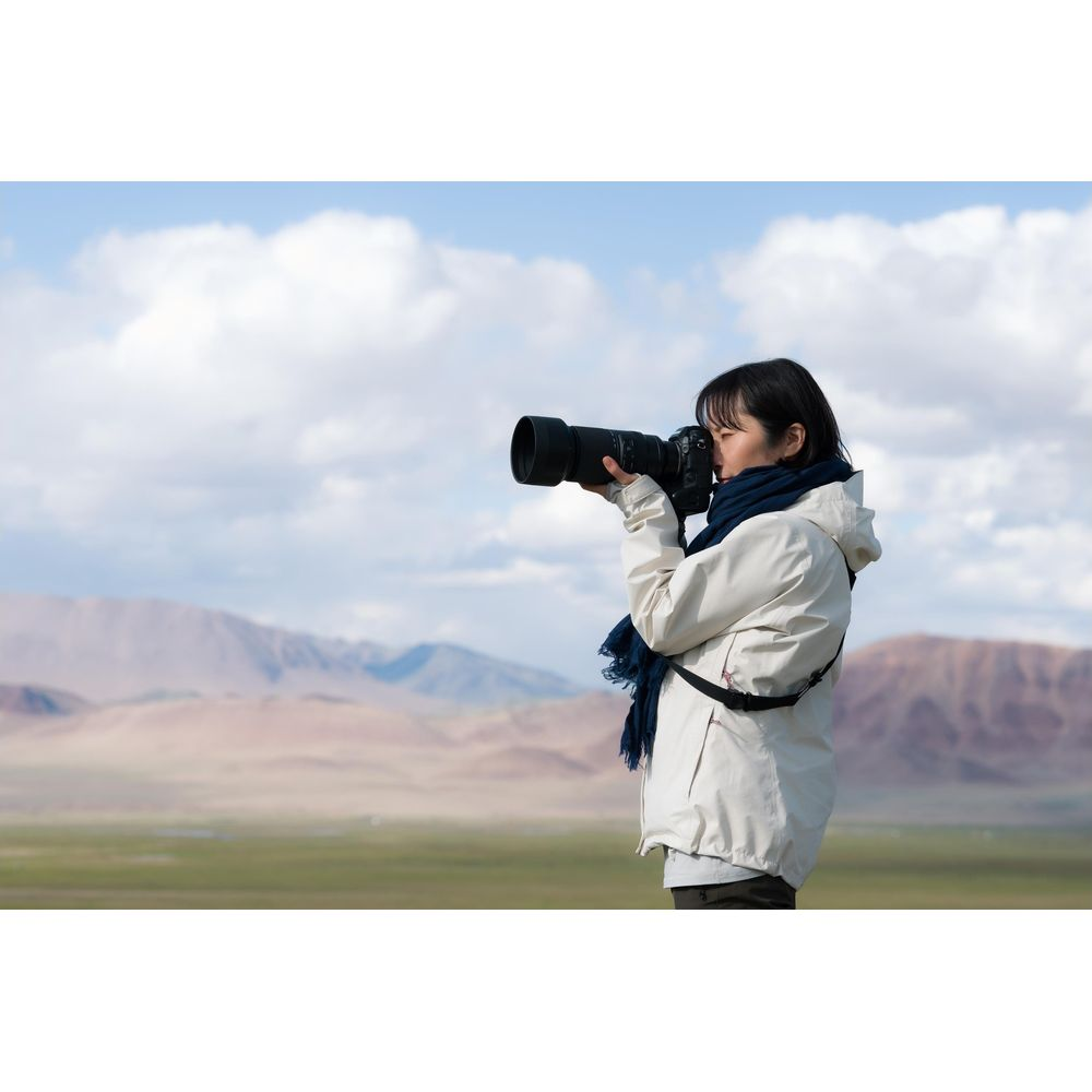 Kobieta fotografuje w górzystym krajobrazie z niebieskim niebem i chmurami.