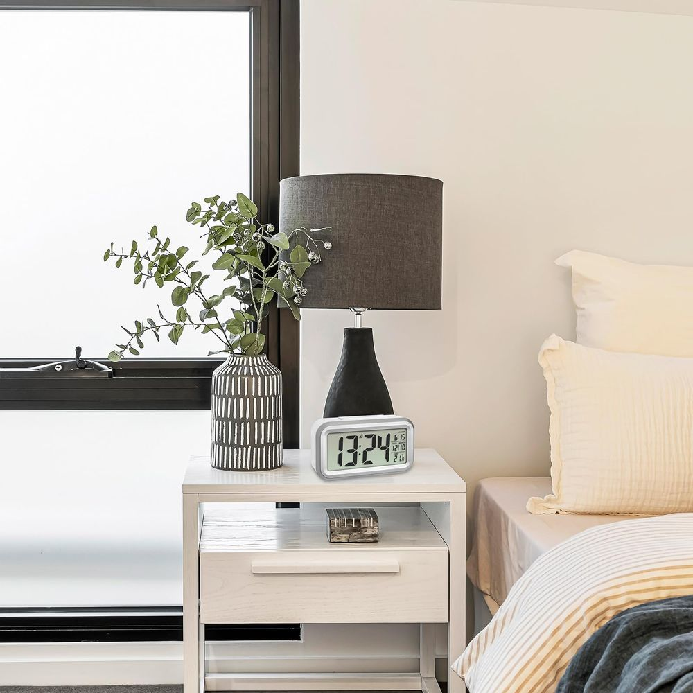 Ein Nachttisch mit Lampe, Vase mit Pflanzen und Digitaluhr.