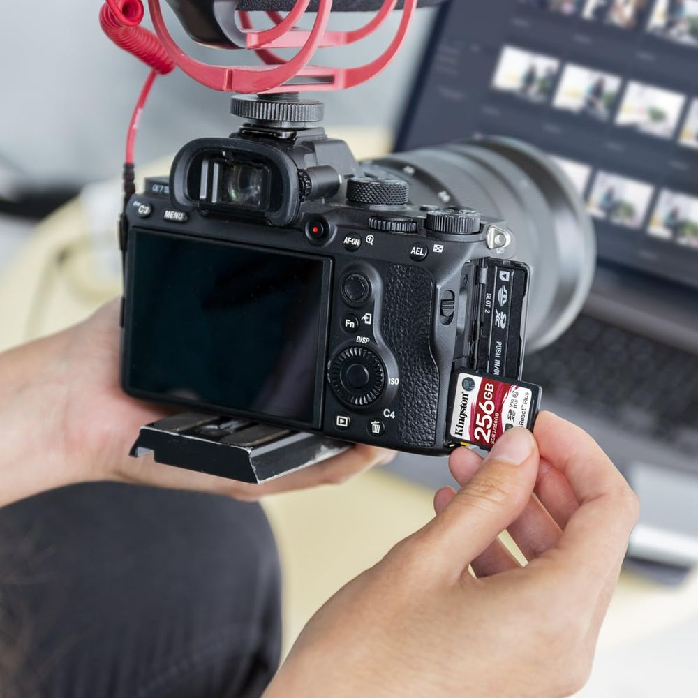 Dłoń wkłada kartę Kingston 256 GB do czarnego aparatu cyfrowego.