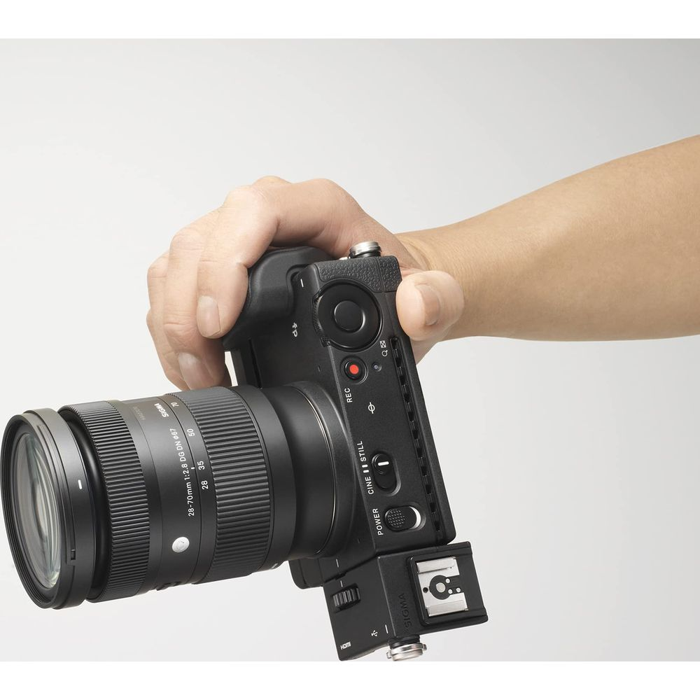 Dłoń trzyma czarny aparat fotograficzny z obiektywem.