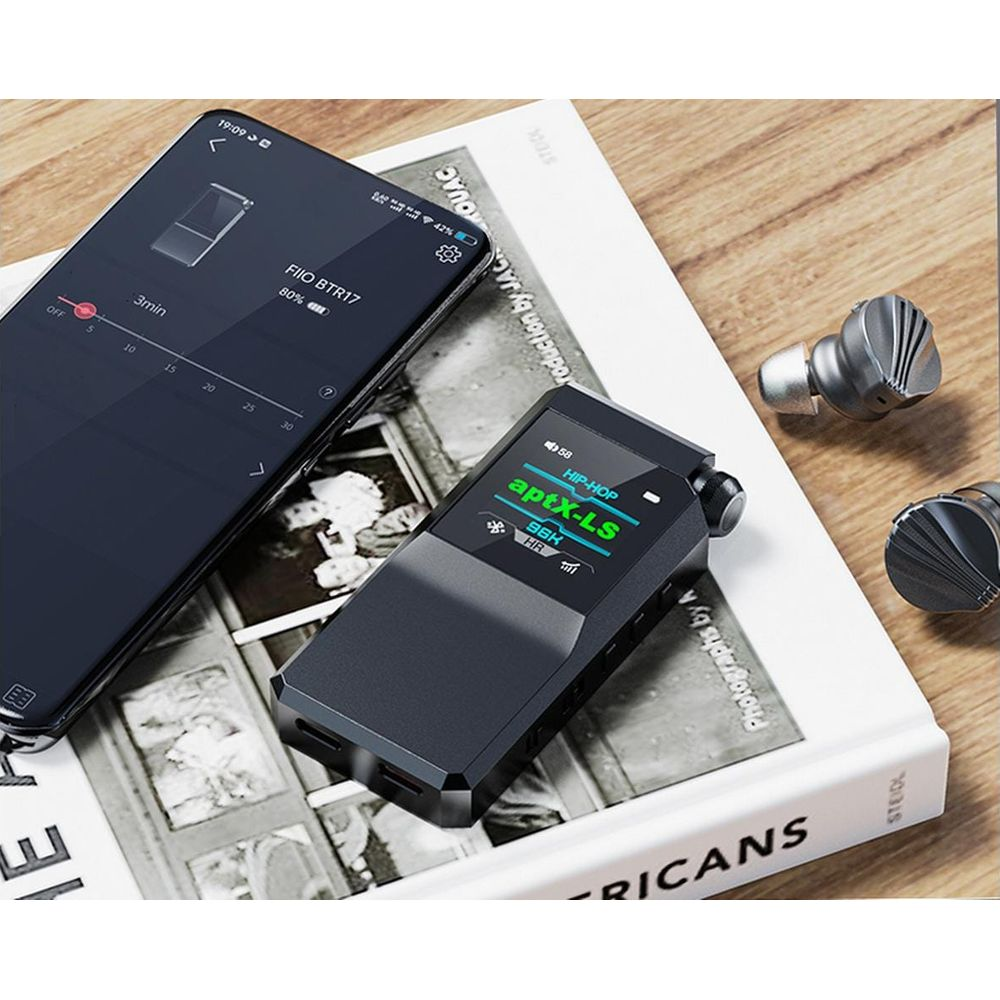 Un FiiO BTR17 negro y un smartphone descansan sobre un libro.