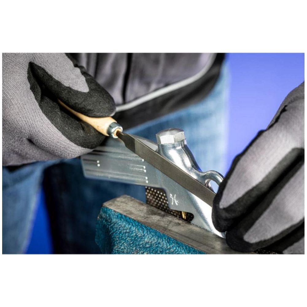 Hände mit Handschuhen feilen an Metallteil in Schraubstock.