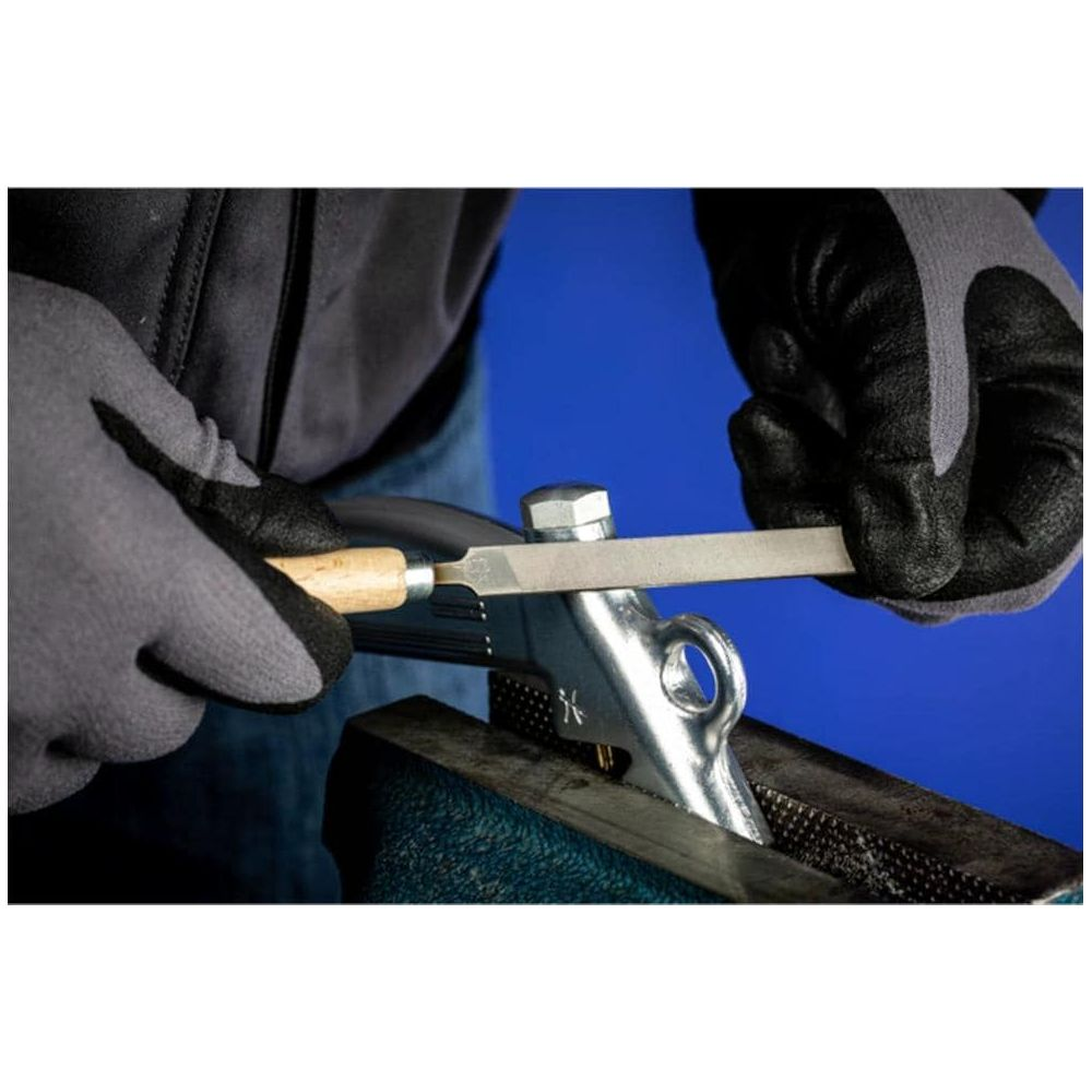 Person mit Handschuhen feilt Metallteil in Schraubstock.