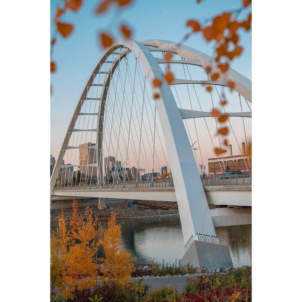Nowoczesny biały most łukowy nad rzeką jesienią z panoramą miasta.