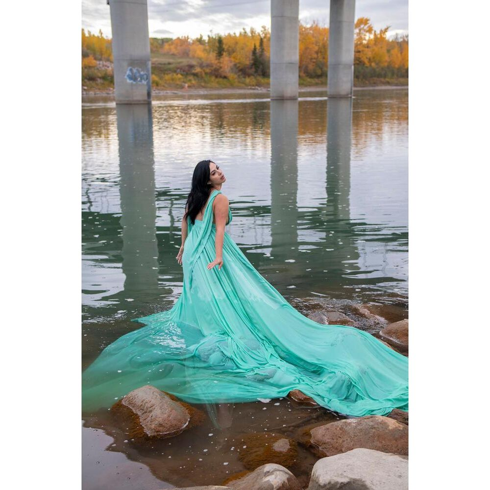 Kobieta w turkusowej sukni stoi w wodzie pod filarami mostu.