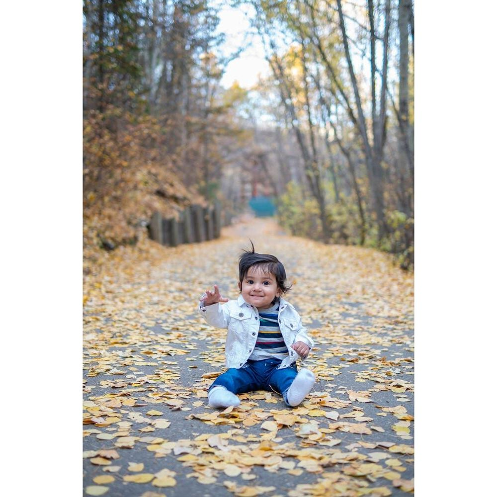 Dziecko siedzi na ścieżce pokrytej jesiennymi liśćmi, w białej kurtce.