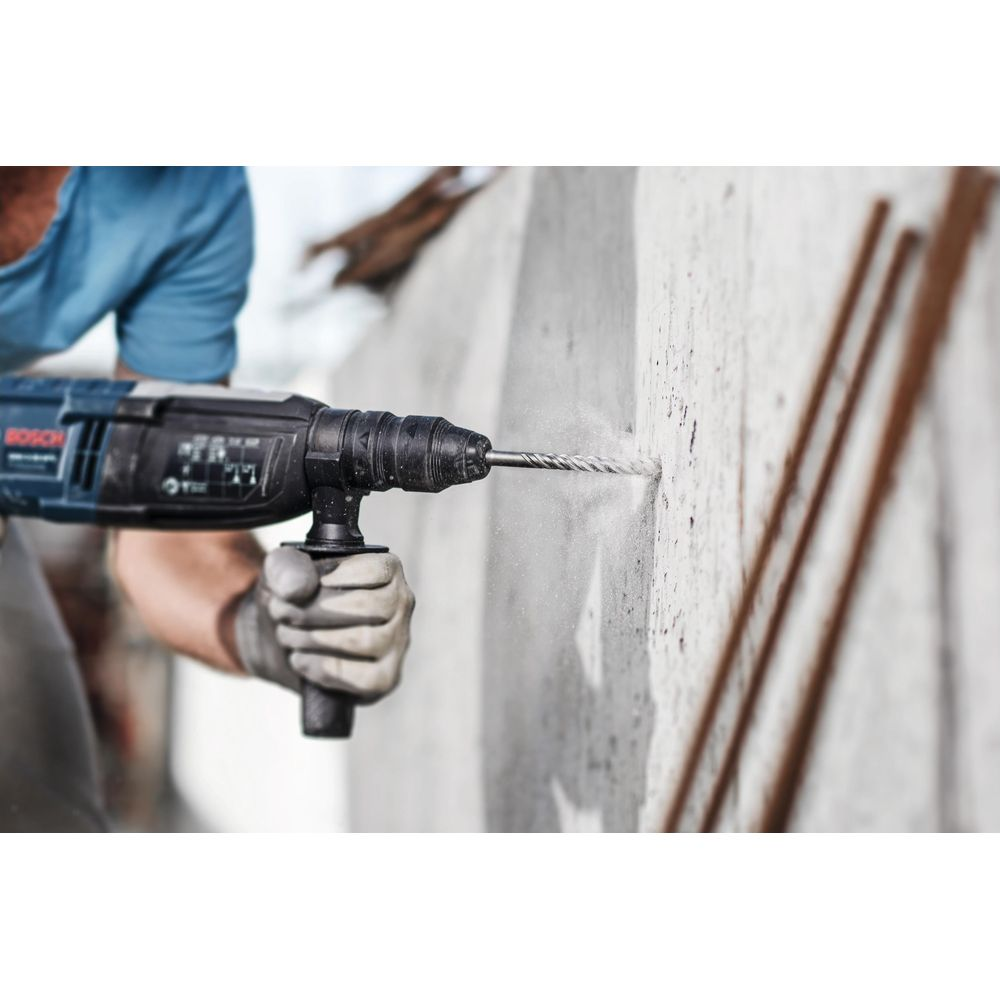 Uomo fora muro in cemento con trapano tassellatore Bosch blu.
