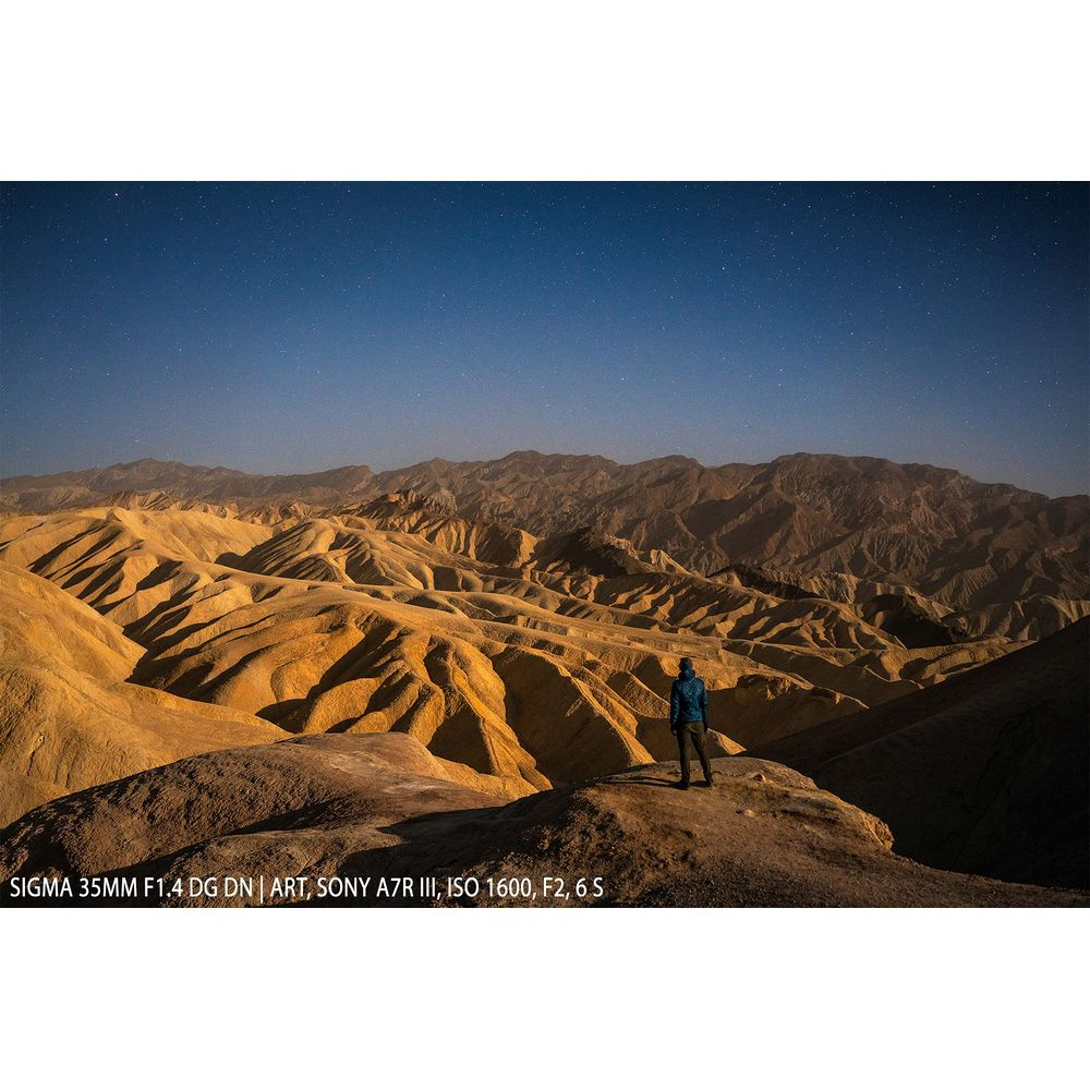 Osoba stoi na wzgórzu, patrząc na pustynny krajobraz pod rozgwieżdżonym niebem.
