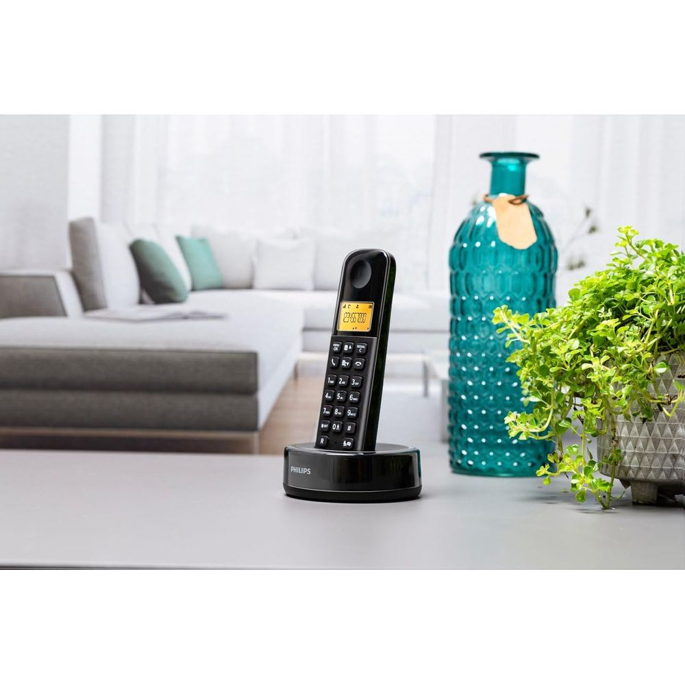 Un téléphone sans fil noir repose sur sa base de chargement. Un canapé à l'arrière.