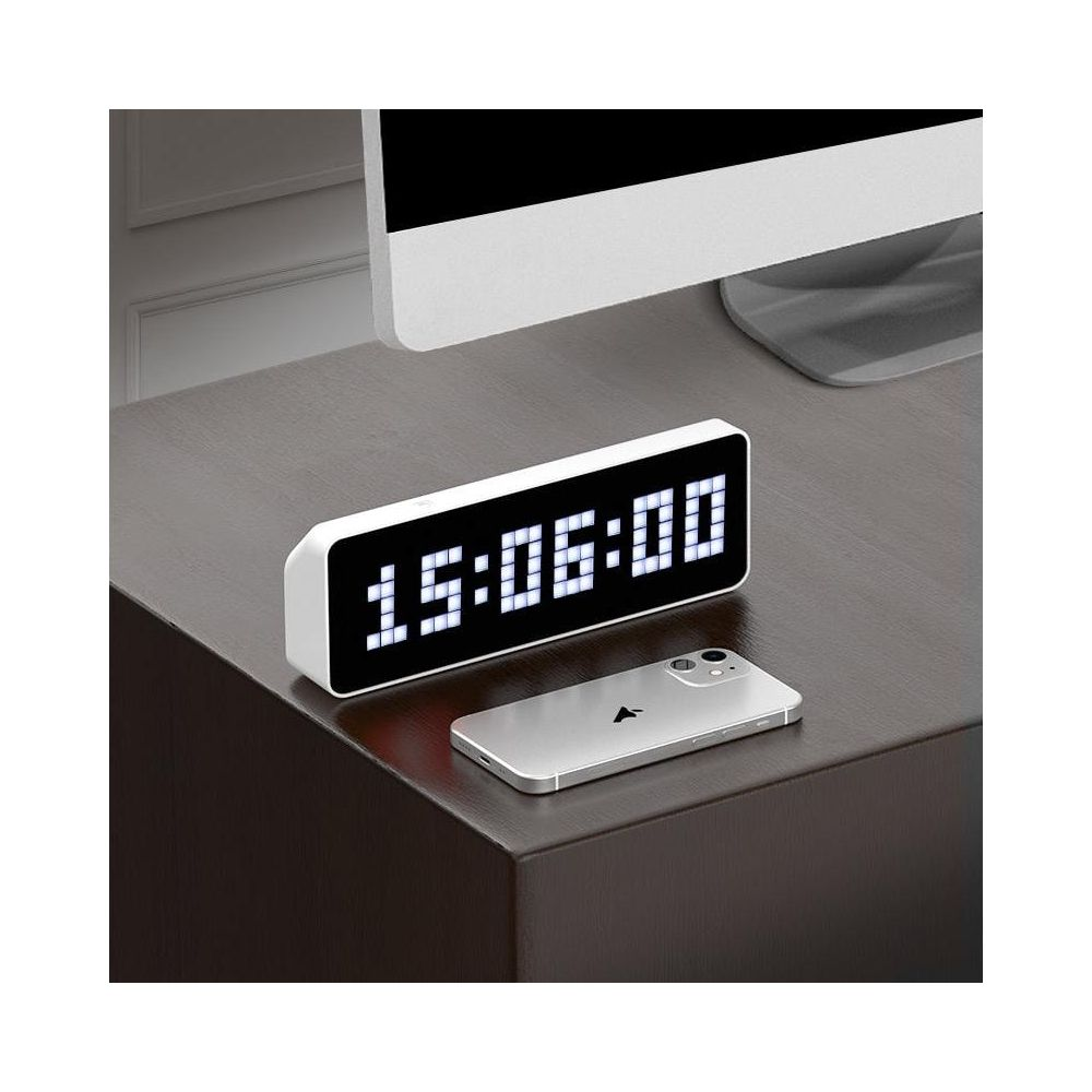 Biały zegar cyfrowy pokazuje 15:06:00, obok leży srebrny smartfon.