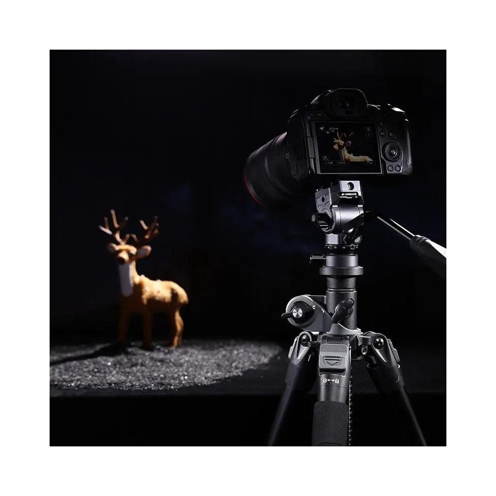 Aparat fotograficzny na statywie z figurką jelenia w tle, ciemne otoczenie.