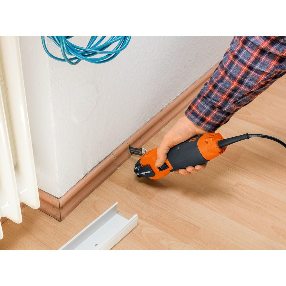 Person schneidet Sockelleiste mit Multitool. Blaue Kabel hängen an der Wand.