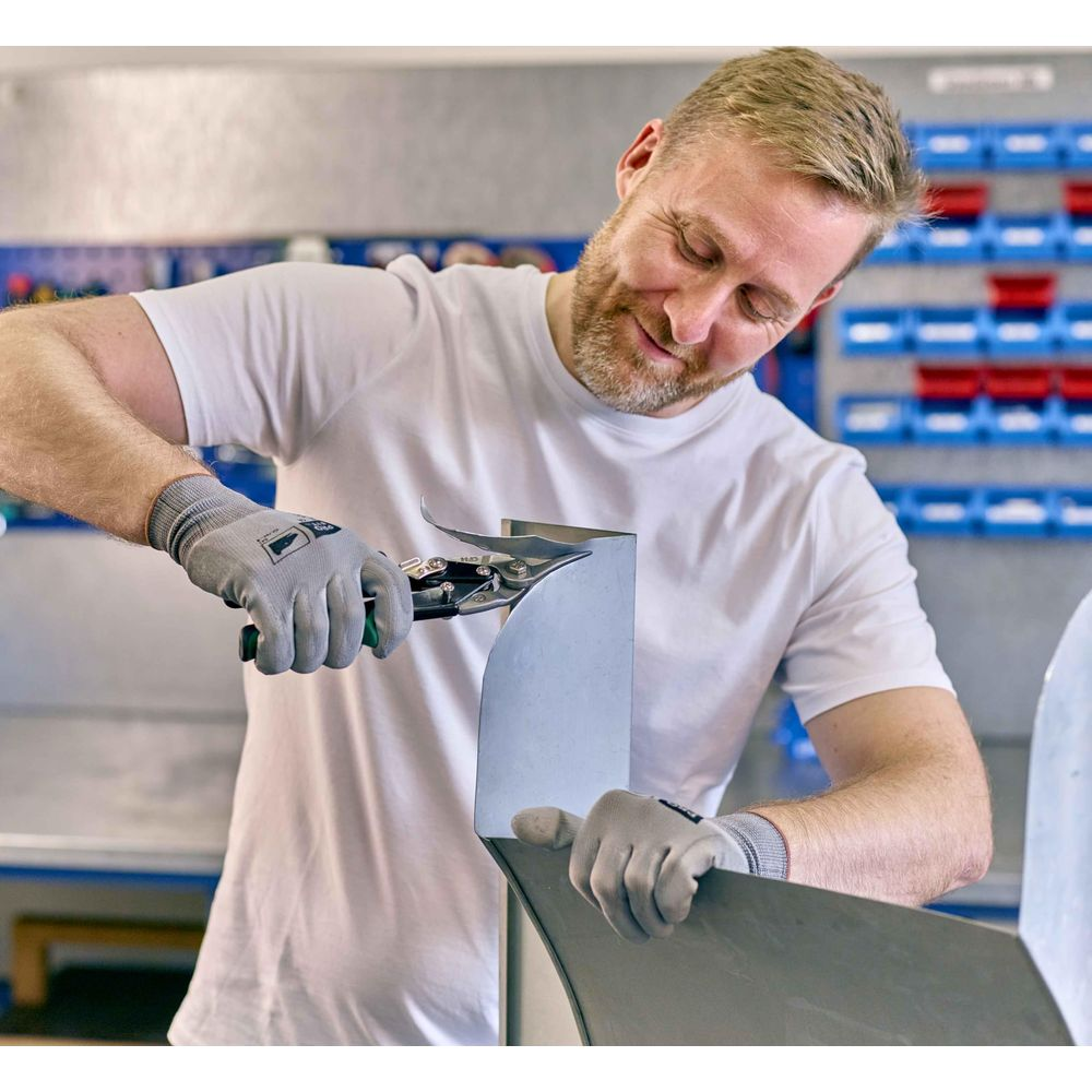 Ein Mann mit Handschuhen schneidet Metall mit einer Zange in einer Werkstatt.