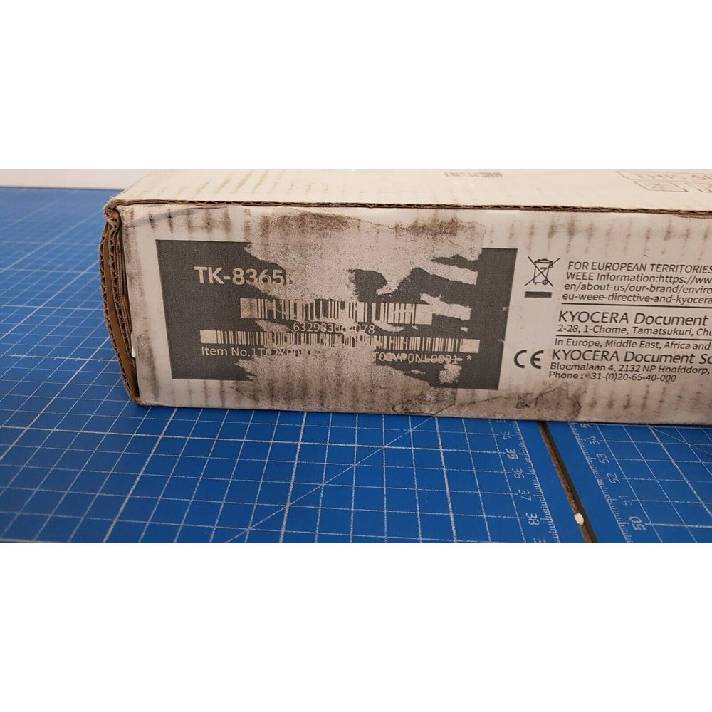 Białe pudełko Kyocera z oznaczeniem TK-8365 i kodami kreskowymi. Niebieska mata pod spodem.