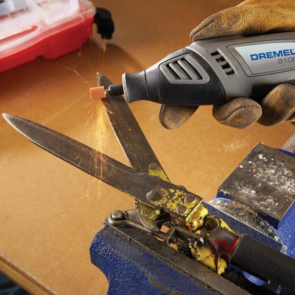 Dremel 8100 szlifuje nożyce w imadle, lecą iskry.