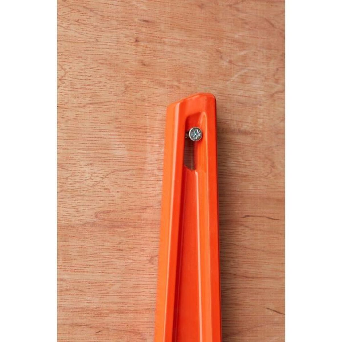 Ein orangefarbenes Plastikteil ist mit einer Schraube an einer Holzoberfläche befestigt.