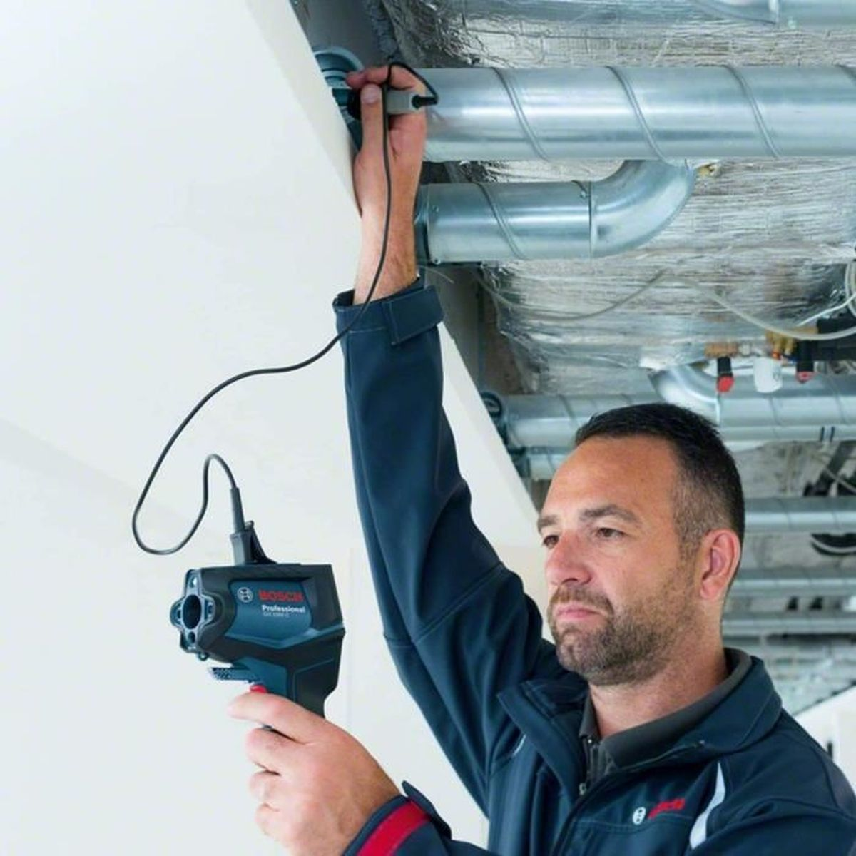 Un uomo ispeziona tubi sul soffitto con un dispositivo di imaging termico.