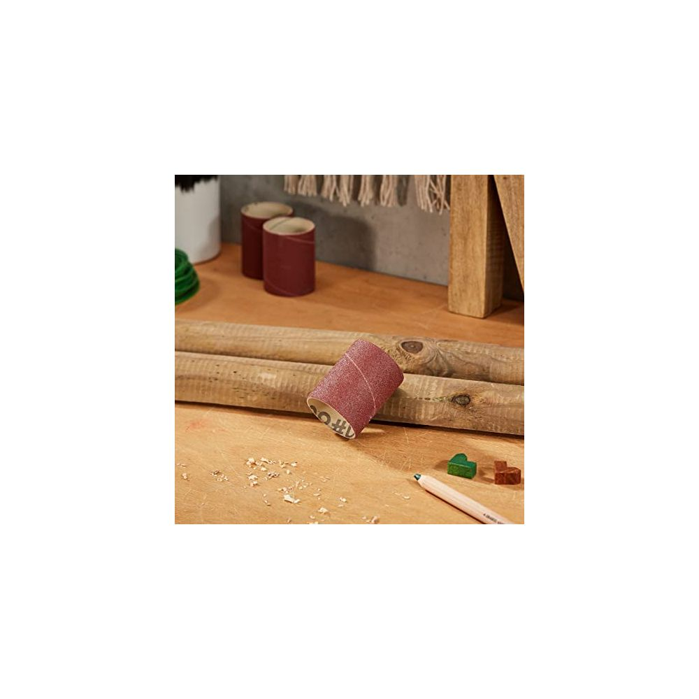 Schleifzylinder liegt auf Holzstämmen, neben Bleistift und Holzstücken.