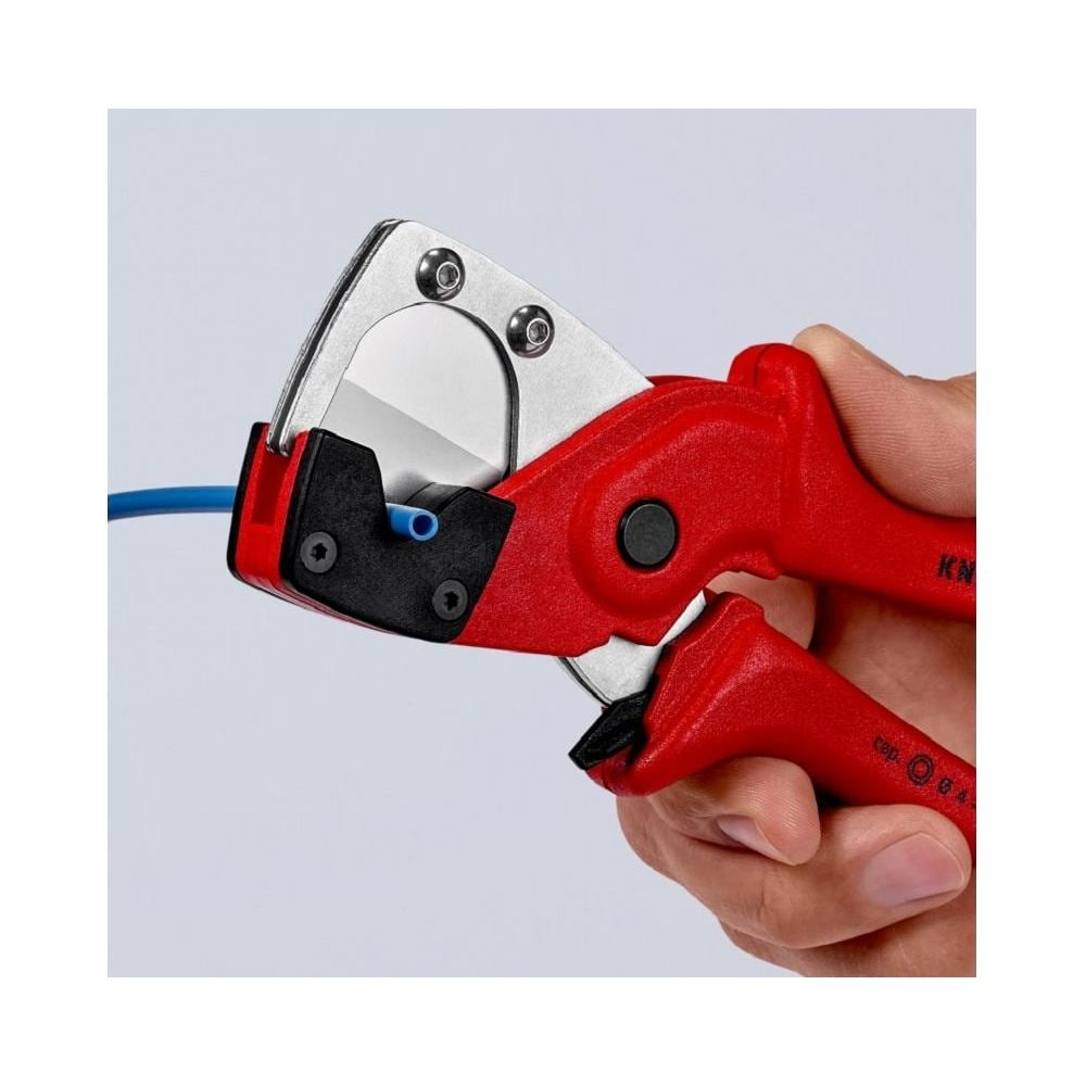 Una mano tiene una pinza tagliatubi rossa, che taglia un tubo blu. Primo piano.