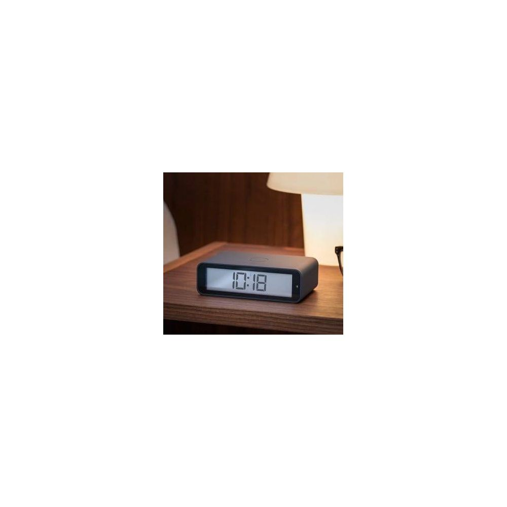 Ein schwarzer digitaler Wecker zeigt 10:18 auf einem Nachttisch.