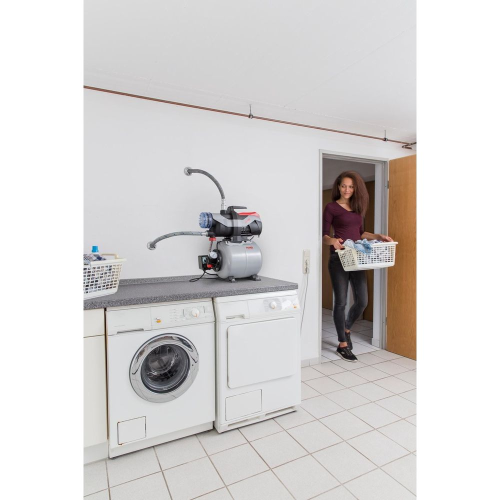 Femme avec panier à linge entre dans la buanderie avec lave-linge, sèche-linge et pompe.
