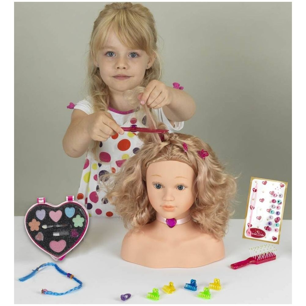 Dziewczynka stylizuje włosy lalki grzebieniem i szczotką. Zestaw do makijażu obok.