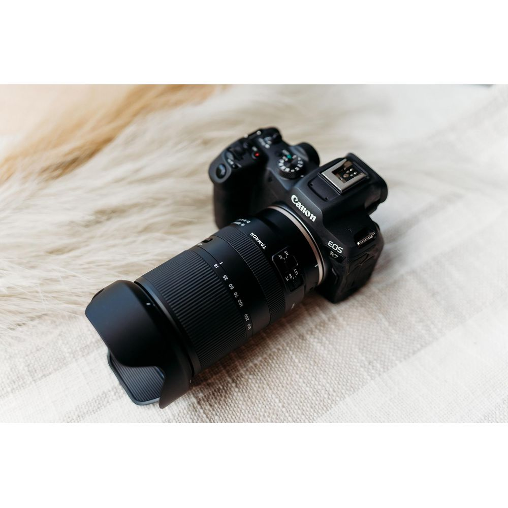 Un appareil photo Canon EOS R7 noir avec un objectif Tamron repose sur un tapis moelleux.