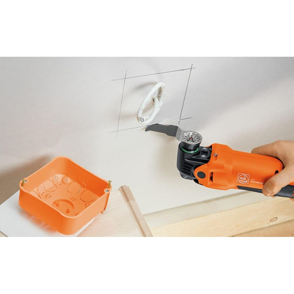 Osoba używa narzędzia do wycinania otworu w ścianie, w pobliżu pomarańczowa puszka elektryczna.