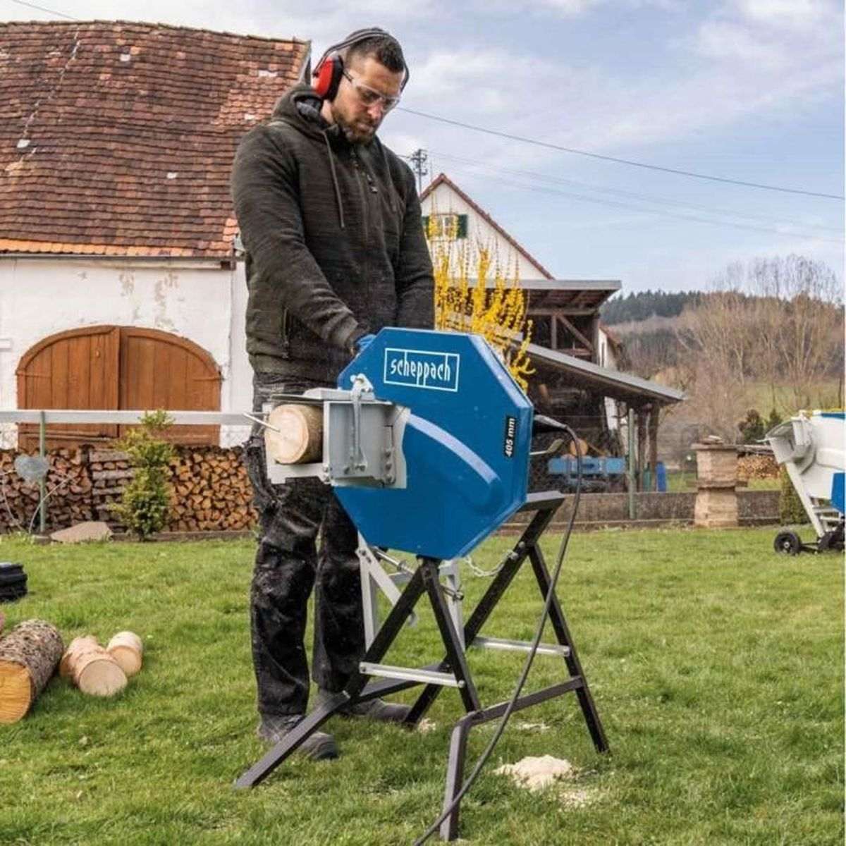 Man met veiligheidsbril en koptelefoon zaagt hout met een blauwe cirkelzaag buiten.