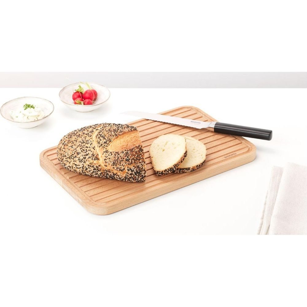 Brot mit Samen, geschnitten, auf einem Holzbrett mit Messer und Beilagen.