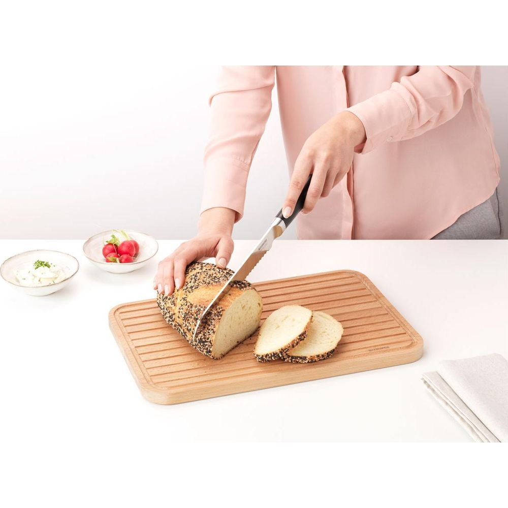 Eine Person schneidet Brot mit einem Brotmesser auf einem Holzbrett. Zwei Scheiben liegen daneben.