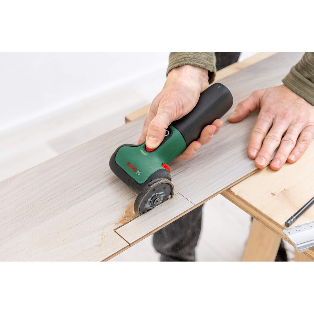 Person schneidet Holz mit einem grünen Bosch-Werkzeug. Staub wird aufgewirbelt.