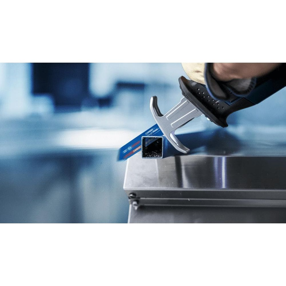 Ręka w rękawicy używa piły szablastowej do cięcia kwadratowej rury metalowej.