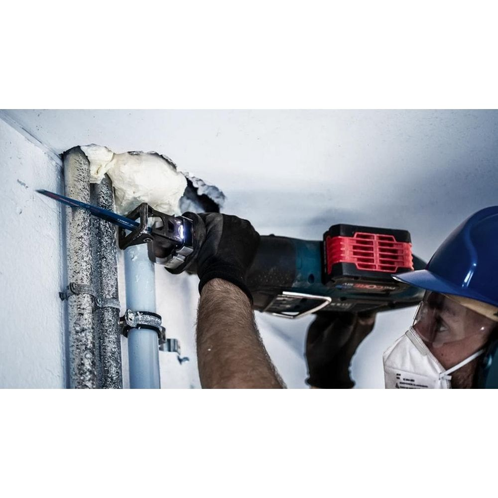 Mężczyzna w kasku i masce tnie piłą szablastą rurę pokrytą pianką.