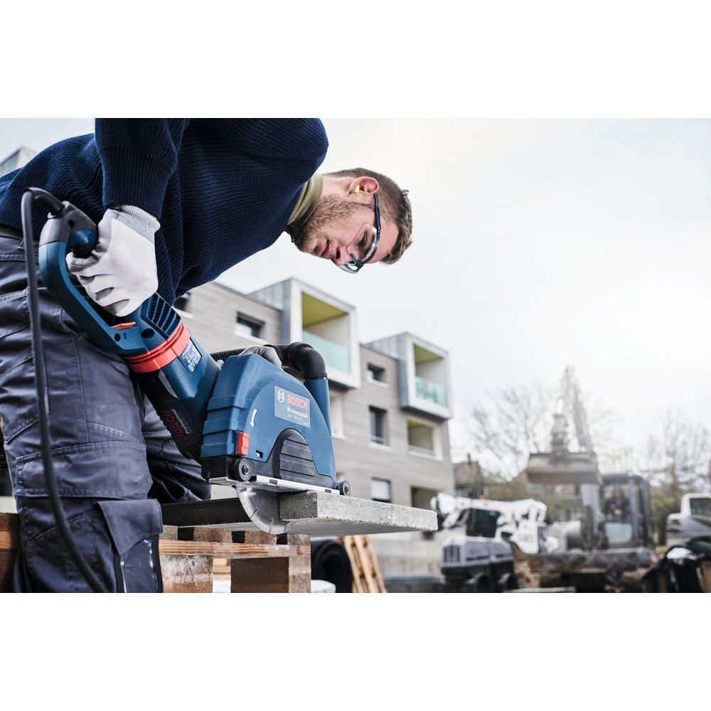 Mann mit Schutzbrille schneidet Stein mit blauer Kreissäge auf Baustelle.