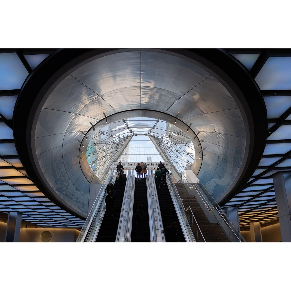 Mensen op roltrappen in een modern gebouw met ronde metaal- en glasarchitectuur.