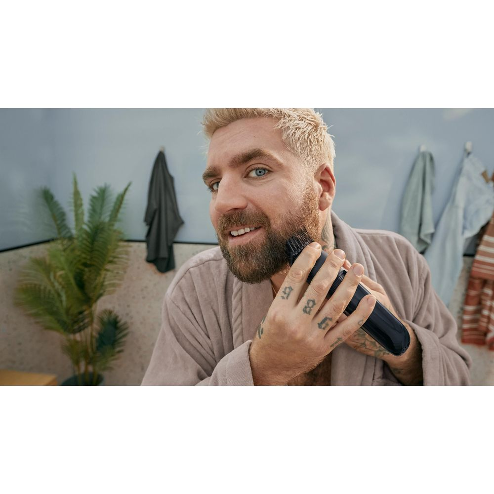 Mężczyzna z blond włosami i brodą używa trymera w łazience.