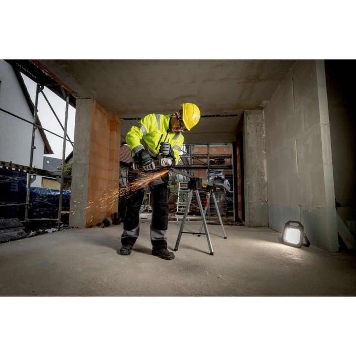 Mężczyzna w żółtej kamizelce i kasku tnie metal na budowie.