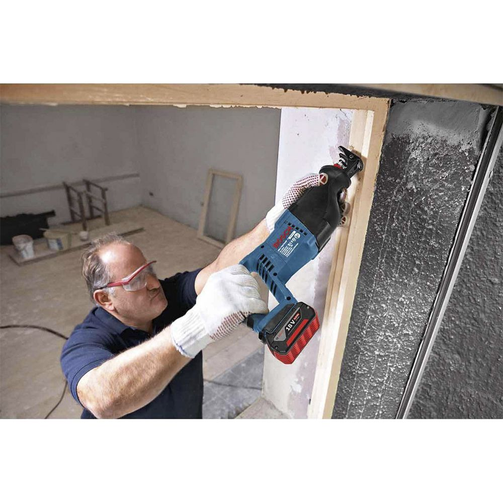 Mężczyzna w okularach ochronnych używa piły szablasto-ramiennej na ramie okna.