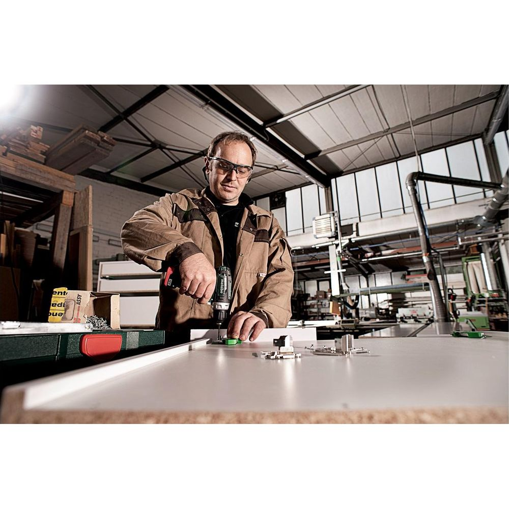 Mężczyzna wierci w desce w warsztacie wiertarką akumulatorową.