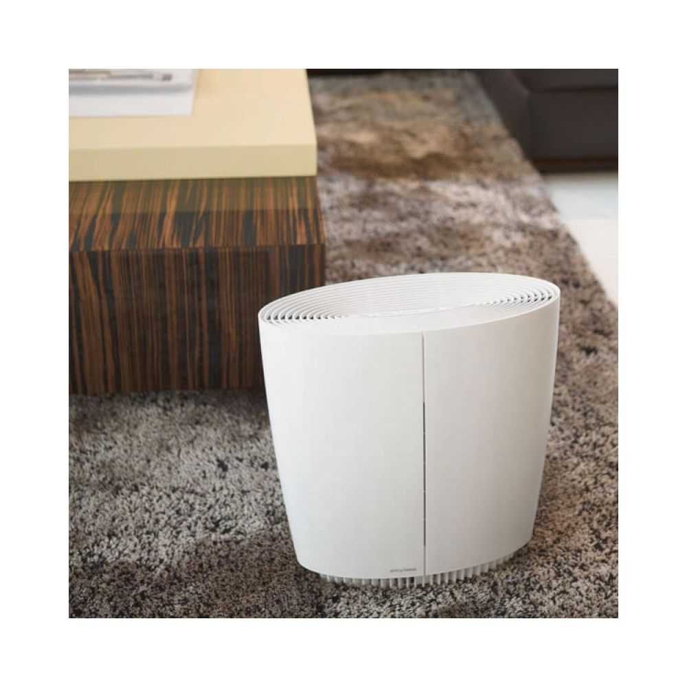 Un purificatore d'aria bianco è seduto su un tappeto soffice accanto a un tavolo di legno.