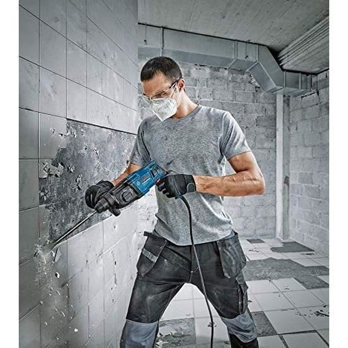 Mężczyzna z wiertarką łamie płytki ścienne.