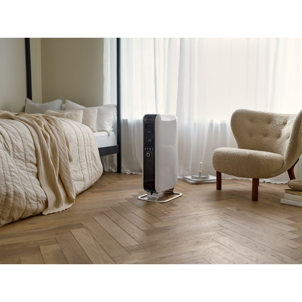 Een witte verwarming staat op houten vloer naast bed en fauteuil.