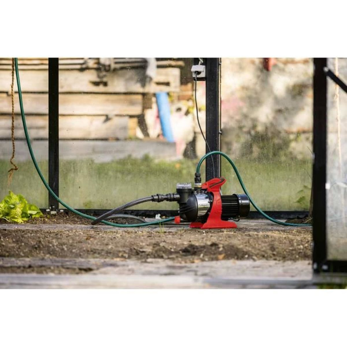 Rote Wasserpumpe mit Schläuchen in einem Gewächshaus auf dem Boden.