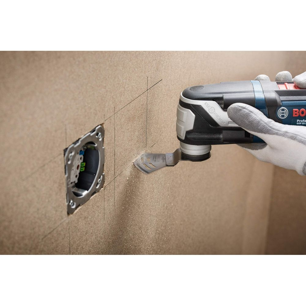 Een persoon gebruikt een multitool om een muur bij een stopcontact te snijden.