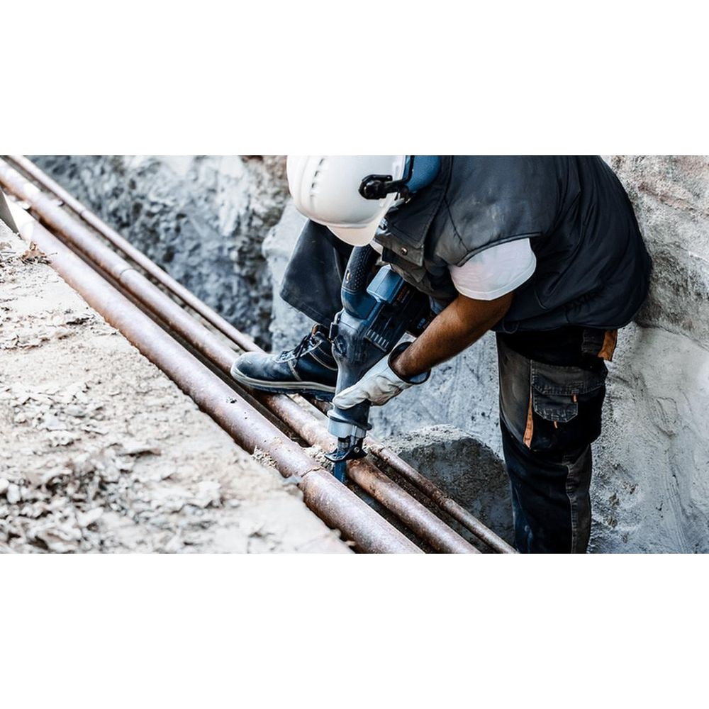 Mężczyzna z wiertarką przy rurach w wykopie.